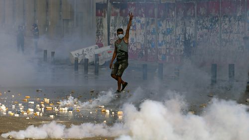 An anti-government protester flashes the victory sign amid tear gas fired by riot police during a protest marking the first anniversary of the massive blast at Beirut's port.