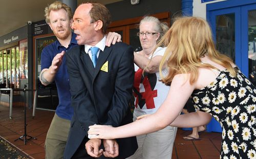 A man dressed as Tony Abbott is hand cuffed during a mock arrest for "attempted eco-cide" at a protest event in Brisbane. (AAP)