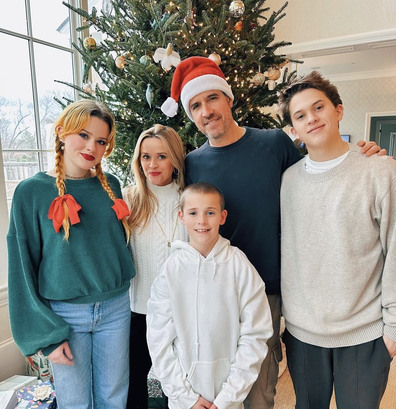 Reece Witherspoon celebrating Christmas 2022 with partner and three kids. Reece Witherspoon and two of the children are wearing beige, her partner is a man in navy jumper and santa hat while her daughter sports blue jeans and a green jumper.