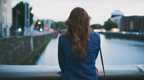 Rear shot of an unrecognizable young woman looking out over the city while standing on a bridge