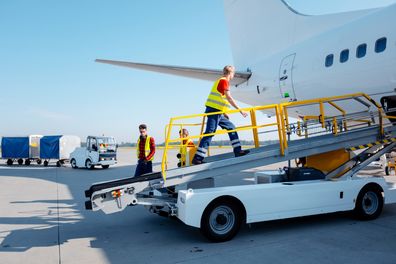 Young men setting the conveyor belt vehicle to the airplane. Airport ground crew at work.