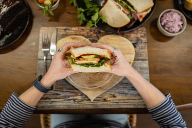 Woman  eating a sandwich that has been plated on a wooden heart shaped board.