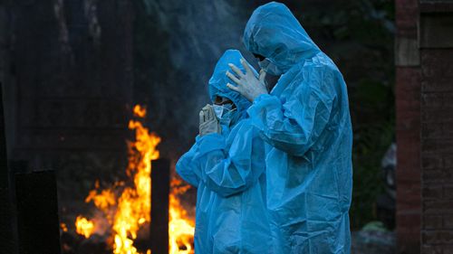 A nine-year-old boy, left, in personal protective equipment offers prayers during the cremation of his father who died of COVID-19 in Gauhati, India.`