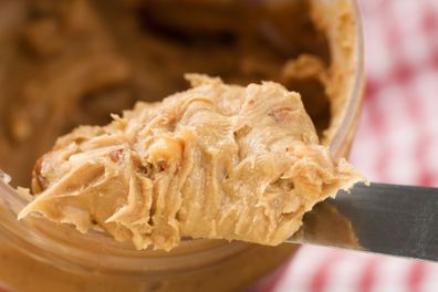 A heap of crunchy peanut butter on a knife coming out of the jar.