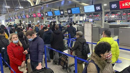 Travellers wearing face masks stand in line at the check-in counters for Cathay Pacific at Shanghai Pudong International Airport in Shanghai.