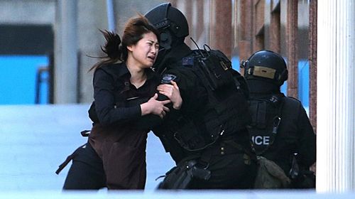 A hostage runs to armed tactical response police officers for safety after she escaped from a cafe under siege at Martin Place. (AAP)