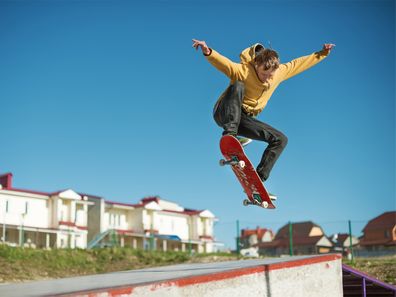 Teenage boy in a yellow hoodie doing a skating trick in mid air.