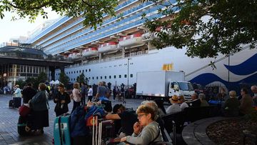 Passengers sit with their luggage after disembarking from the Ruby Princess cruise ship at the Overseas Passenger Terminal in Circular Quay, Sydney.