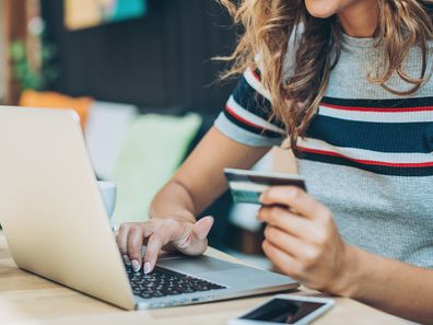 Young woman holding a credit card and typing on a laptop.