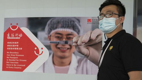 An employee of SinoVac stands near an advertisement for its SARS CoV-2 Vaccine for COVID-19 named CoronaVac at its factory in Beijing on Thursday, Sept. 24, 2020