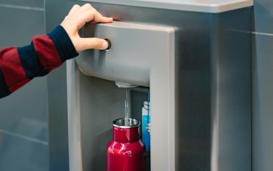 Hand of a traveler pressed the button of drinking water filling station at the Airport