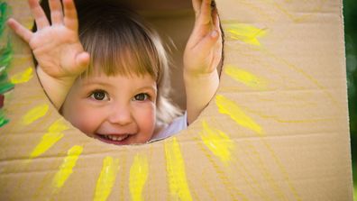 Child looking through a cardboard box with a sun cut-out