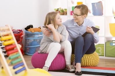 Young speech therapist working with child in colourful educational playroom. Little girl