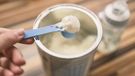 Powder milk for baby and blue spoon on light background close-up. Milk powder for baby in measuring spoon on can. Powdered milk with spoon for baby. Baby Milk Formula and Baby Bottles. Baby milk formula on kitchen background