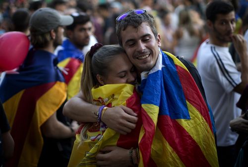 Childhood friends David Jovellar, 24, wearing an 'estelada' or independence flag and Almudena Chueco, 23, wearing a Spanish flag hug as they bumped into each other at a demonstration in Barcelona. (AAP)