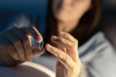 Divorce concept - close up of asian sad depressed woman taking off her wedding ring on the bed