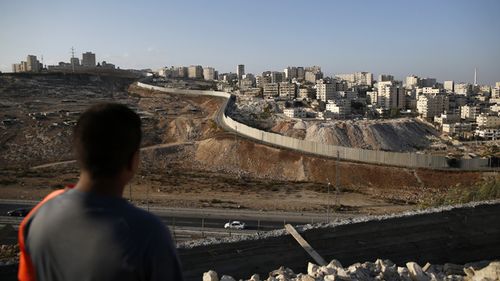 A picture taken on October 18, 2016 from the east Jerusalem Arab neighbourhood of Issawiya shows a Palestinian youth looking on as the Palestinian Shuafat refugee camp (R) is seen behind the controversial Israeli separation wall. 