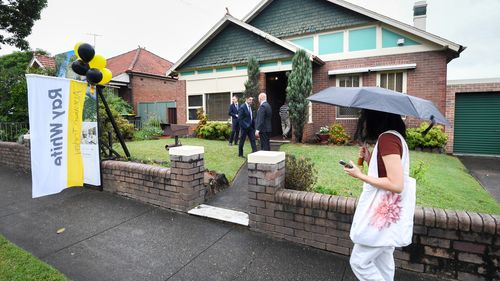 Someone with an umbrella walks past an auction house.