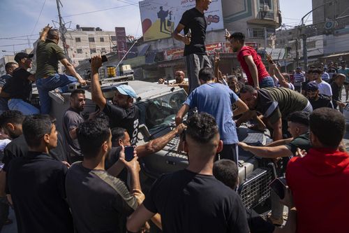 Palestinians gather around an Israeli army vehicle that Palestinian militants drove from Israel into Gaza, in Shejaiya, Gaza Strip, Saturday, Oct. 7, 2023.  