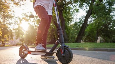 Anonymous waist down image of young man in the park leaning on his electric scooter