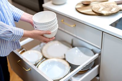 Woman organising clean porcelain plates and bowls in kitchen drawer. Set of plates neatly organised. Tableware storage system in kitchen cabinets
