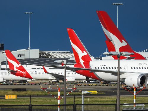 The vertical stabilisers of Qantas planes at Sydney Kingsford-Smith Airport, from the left: a Boeing B737-838 plane, registration VH-XZD; a Boeing B787-9 plane, registration VH-ZNE; and an Airbus A380-842 plane, registration VH-OQB. In the background on the left is a fourth Qantas plane, a Boeing B737-838, registration VH-XZH. In the far background is the international terminal.  In the foreground are navigational light structures at the northern end of the runway.  This image was taken from Nig