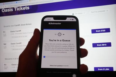 A person in a queue to access the Ticketmaster website on their phone, with the StubHub website in the background, detailing information about Oasis concert tickets for sale, in London.