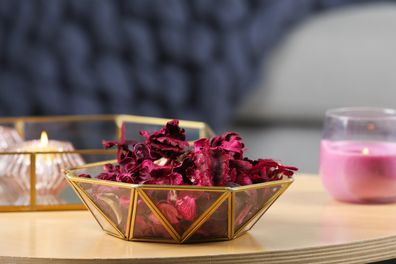 Aromatic potpourri of dried flowers in decorative bowl and burning candles on table indoors, space for text