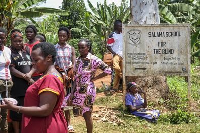 Relatives and other villagers wait near the scene of a fire at the Salama School for the Blind in Luga village, Mukono district, Uganda Tuesday, Oct. 25, 2022.