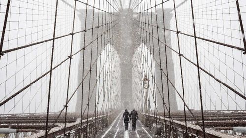Pedestrians shiver while crossing the Brooklyn Bridge in New York. (AAP)