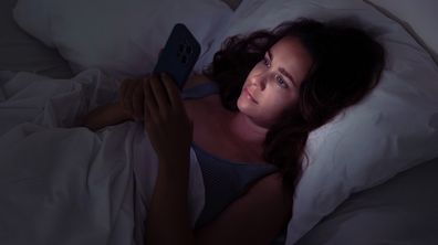 Woman laying in bed at night looking at her phone