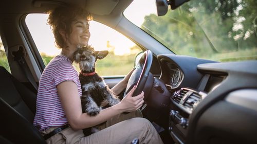 Beautiful young woman enjoying road trip with her cute schnauzer.
