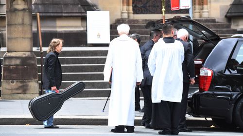 Angus Young carries a guitar as he watches the casket of his brother, AC/DC co-founder and guitarist Malcolm Young, get carried from St Mary's Cathedral in central Sydney to a waiting hearse (Image: AAP)