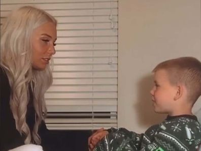 Mum and young son sitting in bed, facing each other and holding hands.