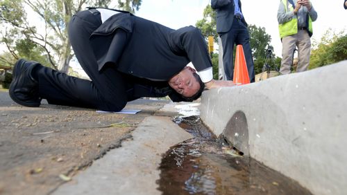 Nick Xenophon is seen looking into a gutter to view the new storm water saving system, ahead of a press conference at the Waite Institute in Adelaide. (AAP)
