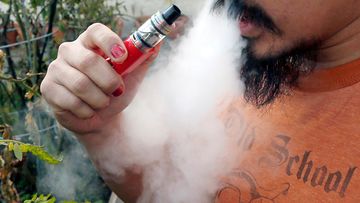 A man blows a puff of smoke as he vapes with an electronic cigarette.