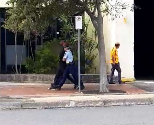 Another man was escorted away by police in handcuffs. (9NEWS)