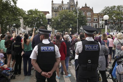 Police officers watch members of the public outside the Town Hall in Southport