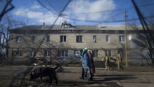 Two Ukrainian soldiers patrol a street as elderly women walk past a house damaged by artillery shelling in Novoluhanske, eastern Ukraine amid the threat of a Russian invasion. 