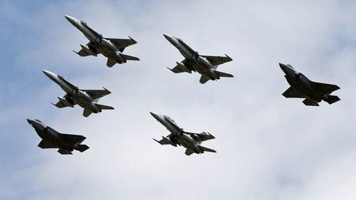 Two F-35A Joint Strike Fighters flank FA 18 aircraft ion a flyover at Williamtown RAAF Base. 