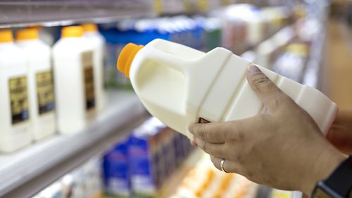 Close up of a man's hand picking up a bottle of organic fresh milk from the dairy aisle in supermarket. Healthy eating lifestyle and routine.