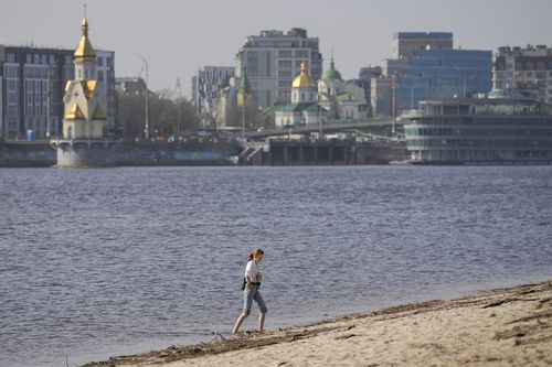 A woman enjoys a warm afternoon on the bank of the Dniepr River in Kyiv, Ukraine, Tuesday, April 2, 2024.  