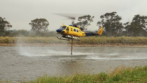 In this photo provided by Costi Farms a helicopter refills it's tank to help fight a wildfire as it moves through Deepwater National Park