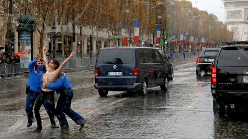 A topless woman is tackled by police as she runs towards President Donald Trump's motorcade in Paris.