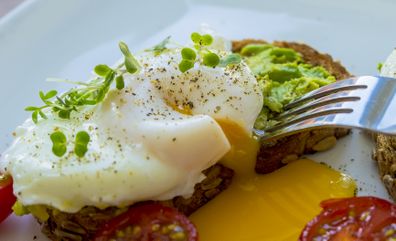 Poached egg on Rye bread being cut up revealing a runny yolk, cress on top, tomatoes,