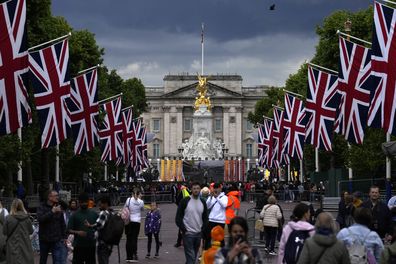 People stand on The Mall looking towards Buckingham Palace and the Queen Victoria Memorial statue as the road is lined with Union flags and closed to traffic ahead of Britain's Queen Elizabeth II's Platinum Jubilee, in London, Tuesday, May 31, 2022. 
