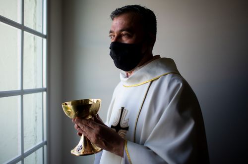 Father Andres Arango distributes Holy Communion while wearing a mask amid the COVID-19 pandemic at Gordon Hall at St. Gregory's Catholic Church in Phoenix on May 10, 2020. St. Gregory's Catholic Church Communion COVID-19