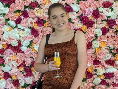 Caitlin Magagna poses in front of a wall of flowers.