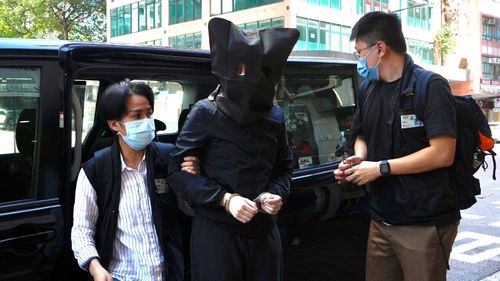 A hooded suspect is accompanied by police officers in Hong Kong