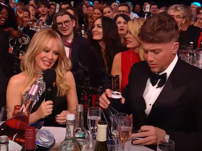 Kylie Minogue and Roman Kemp do a shoey during the 2024 Brit Awards